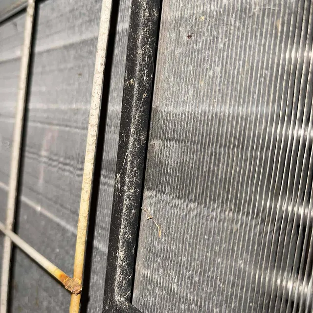 Nærbilde av skittent og støvete varmepumpefilter med rustflekker på metallgitteret.