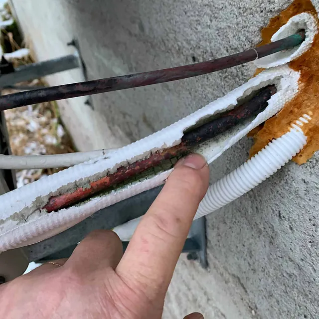 Hånd peker på skadet og rustet rørisolasjon på en varmepumpeinstallasjon.